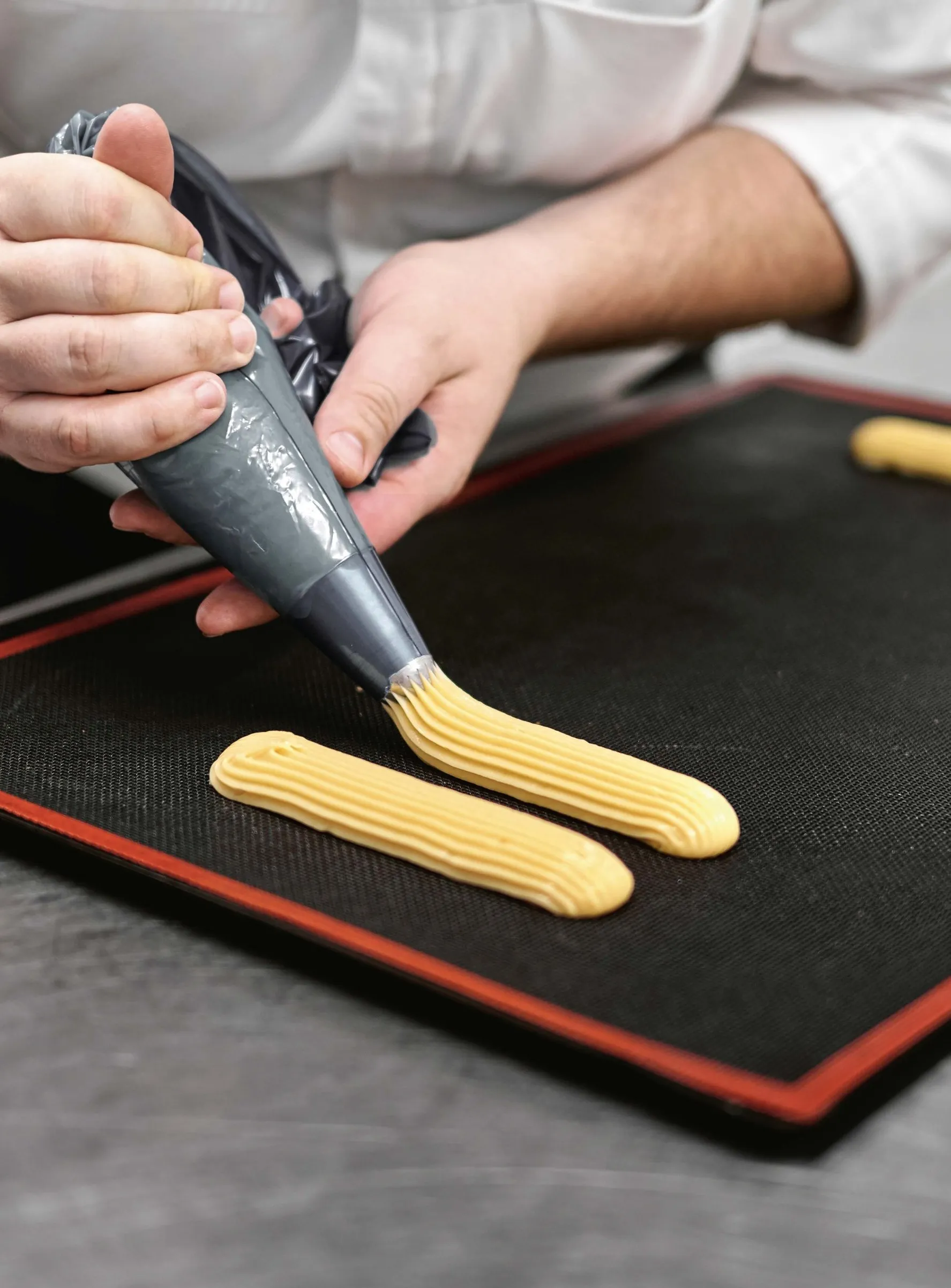 Des mains garnissent des éclairs au chocolat à l’atelier BO&MIE