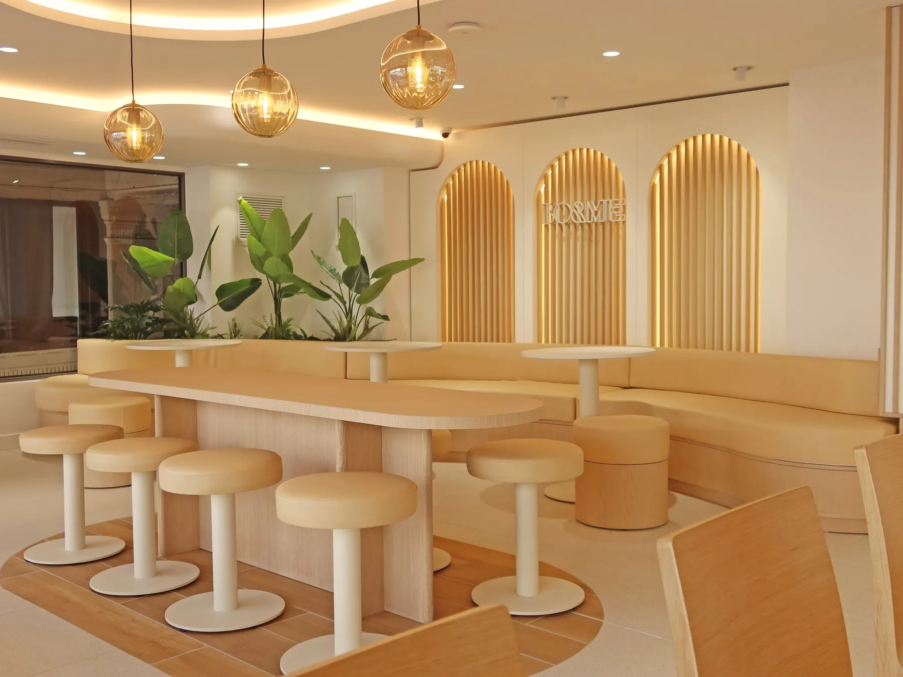 La salle d’une boutique BO&MIE : banquette courbe, tabourets et arches lumineuses