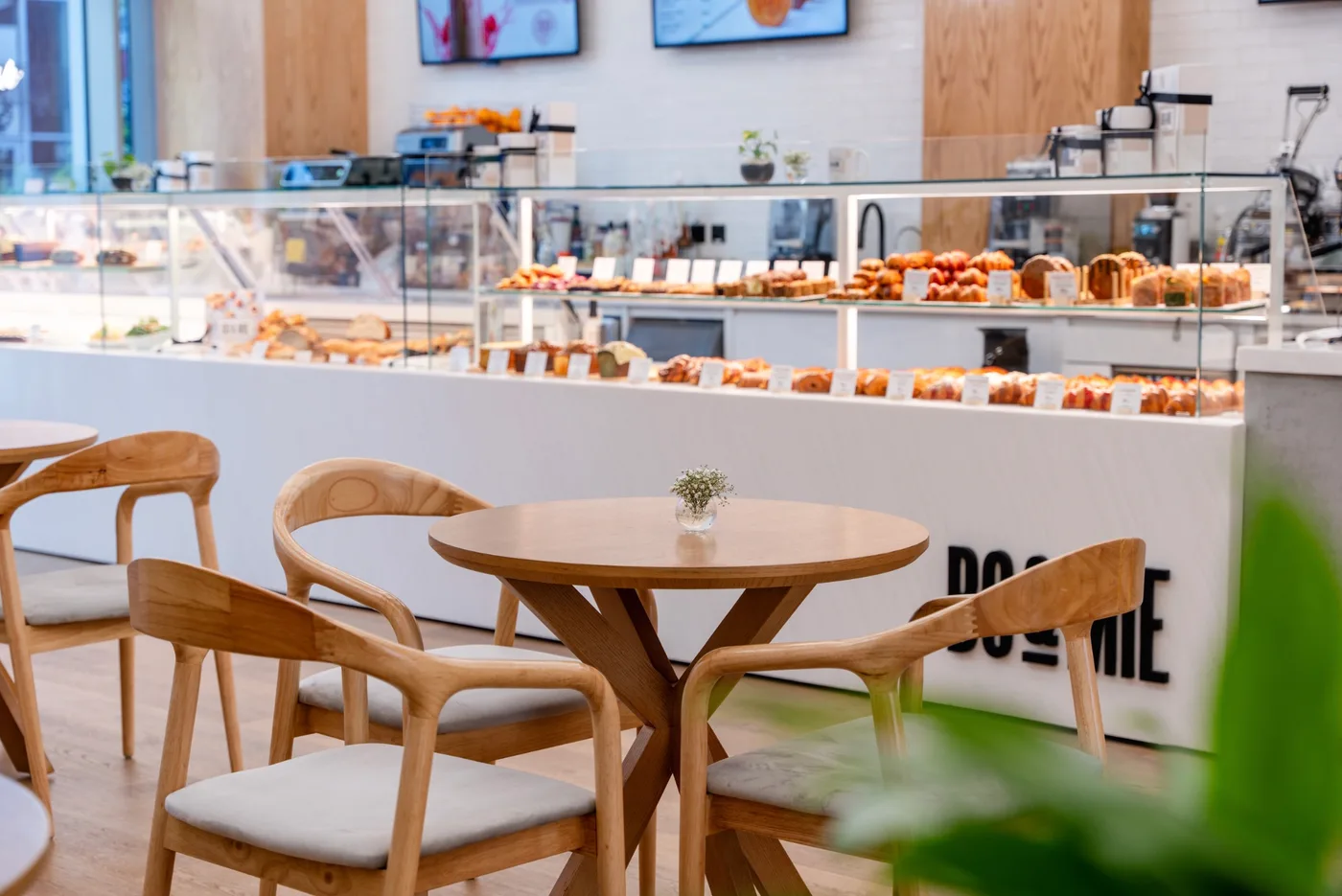 La salle de BO&MIE Djeddah : tables rondes et fauteuils de bois clair, comptoir blanc frappé du logo BO&MIE, vitrines de viennoiseries et de pâtisseries
