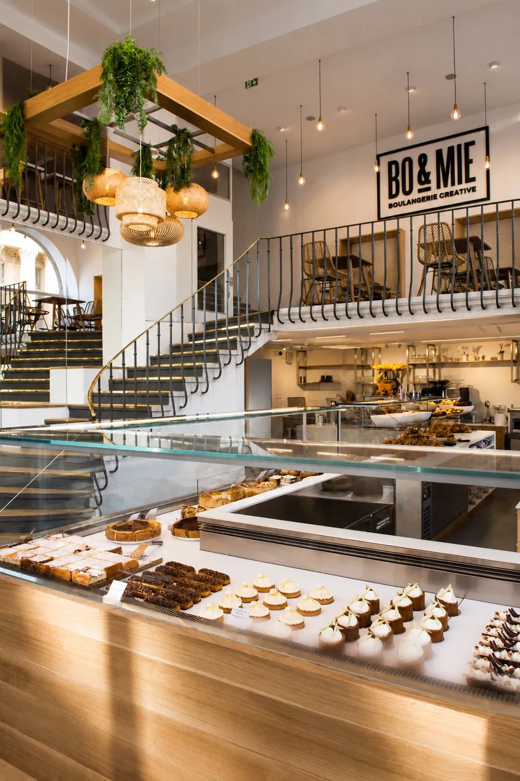 L’intérieur de BO&MIE Louvre-Rivoli : l’escalier en fer forgé qui monte vers la mezzanine, au-dessus du long comptoir de pâtisseries