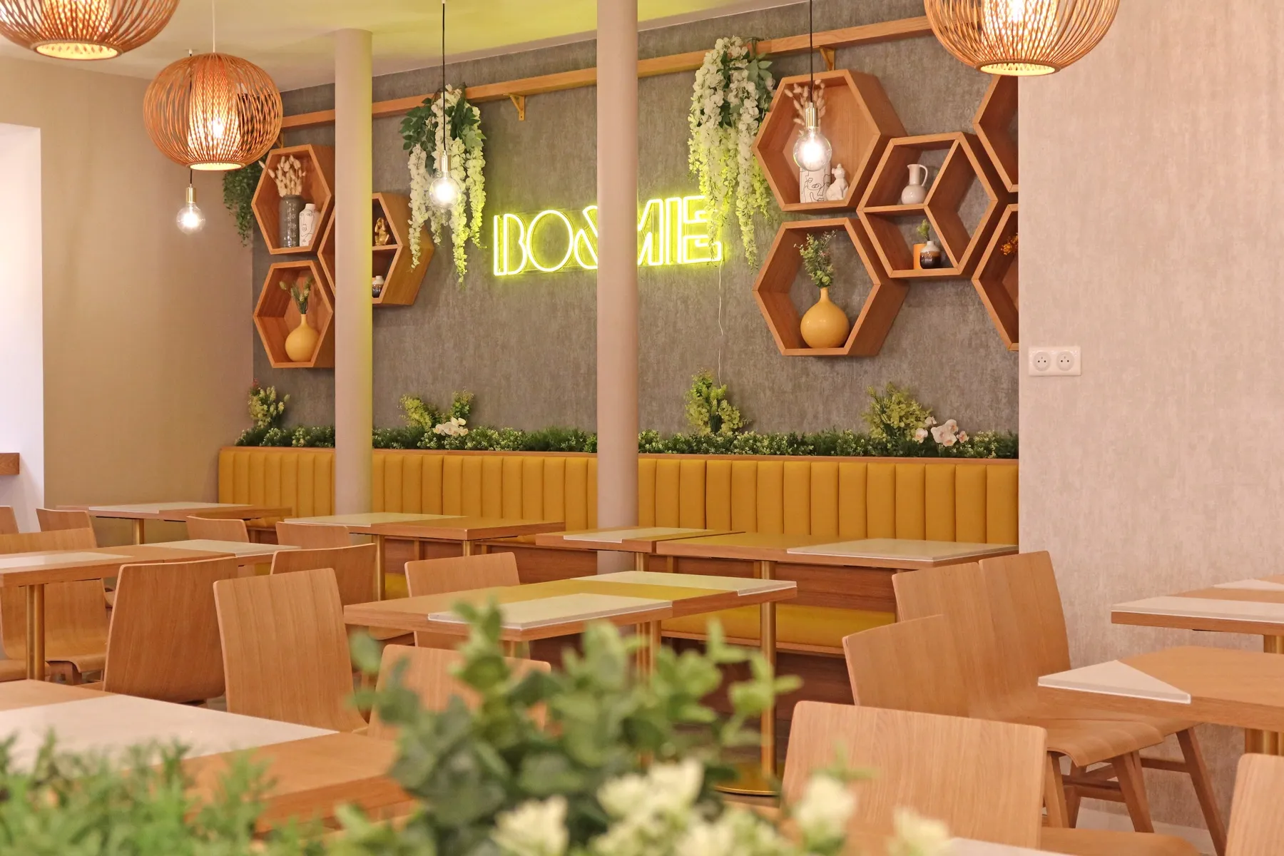 La salle de BO&MIE Saint-Michel : le néon BO&MIE au mur, banquettes jaunes, niches hexagonales en bois et feuillages suspendus