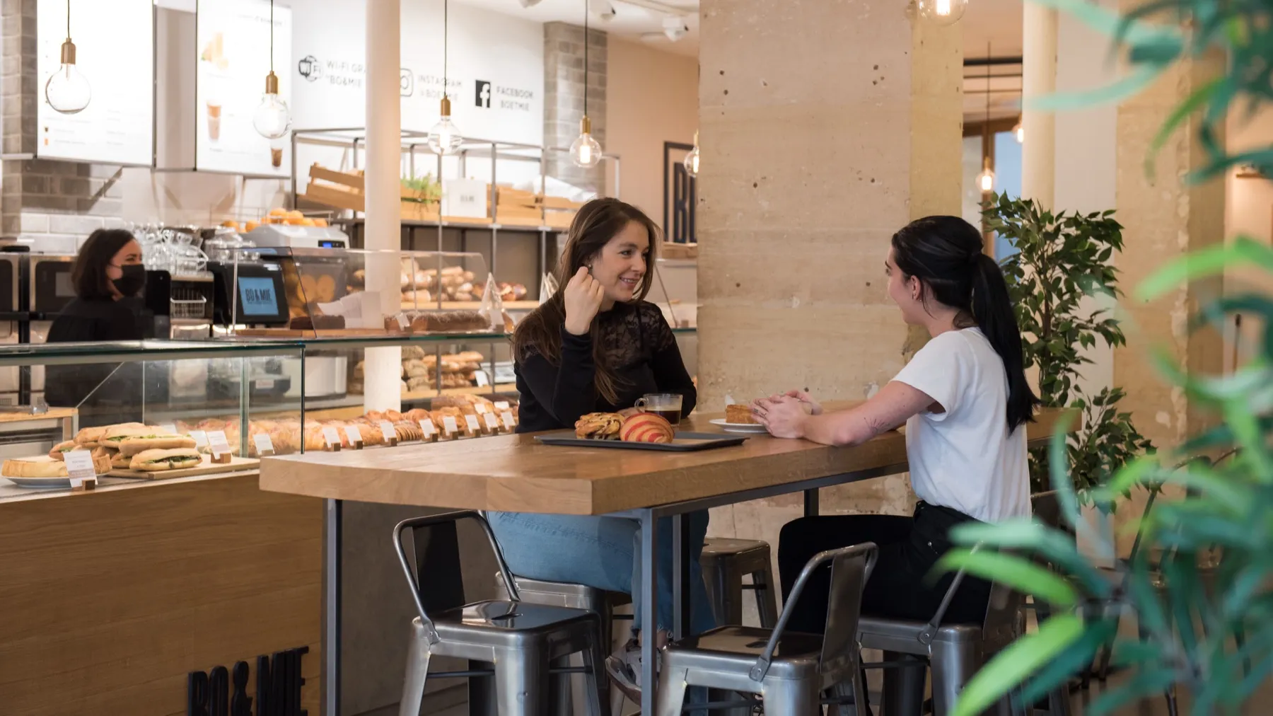 La salle de BO&MIE Turbigo : deux clientes attablées devant le comptoir à pains, sous les suspensions