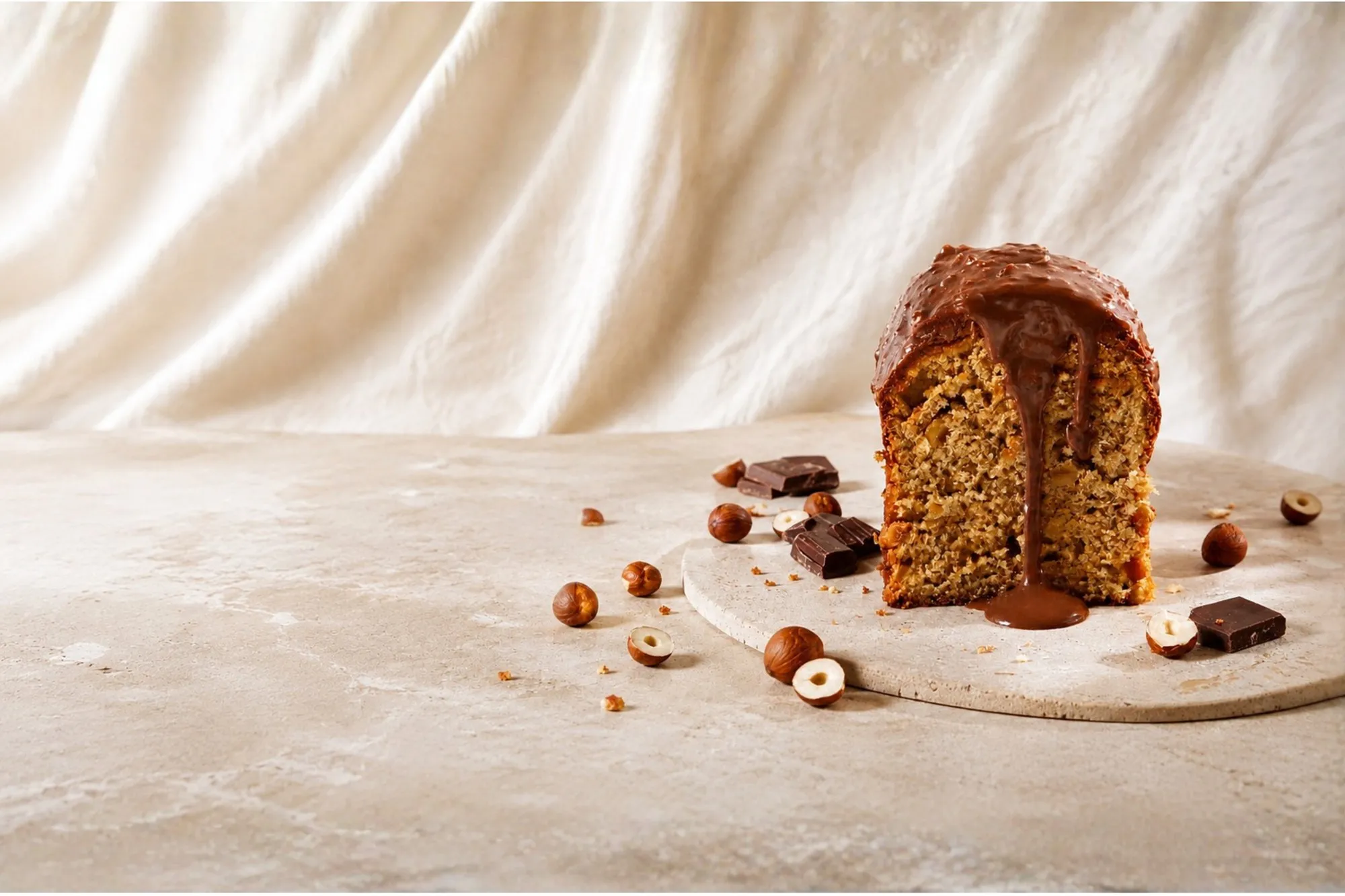 Un cake noisette BO&MIE tranché, glaçage chocolat coulant, noisettes et carrés de chocolat autour