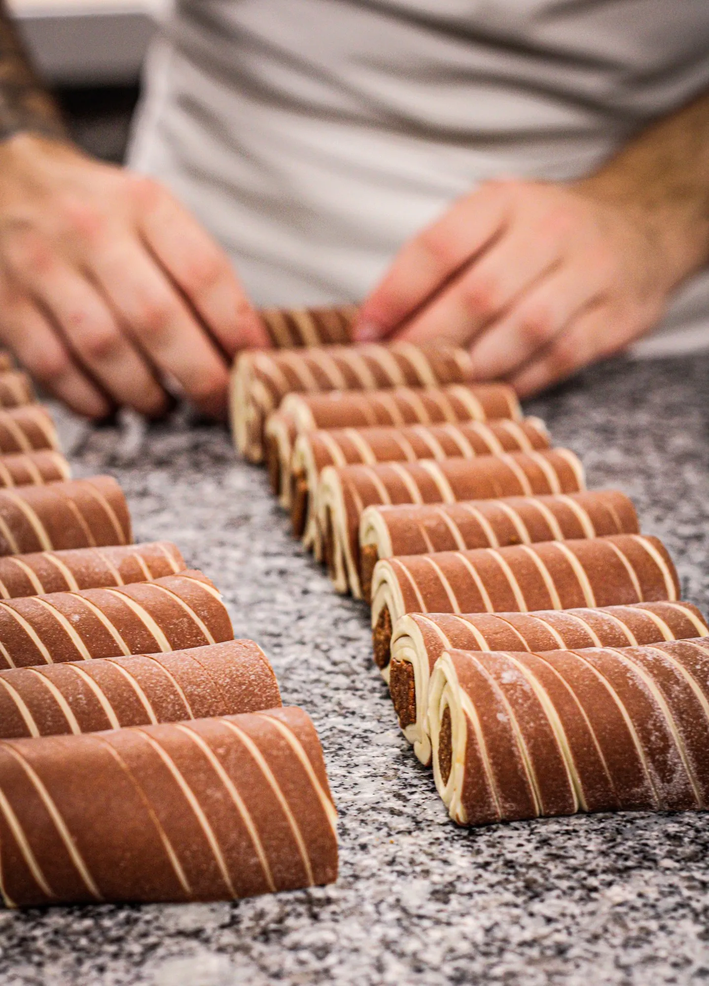Les mains d’un tourier alignent les pains au chocolat crus, en rangées sur le plan de travail en granit