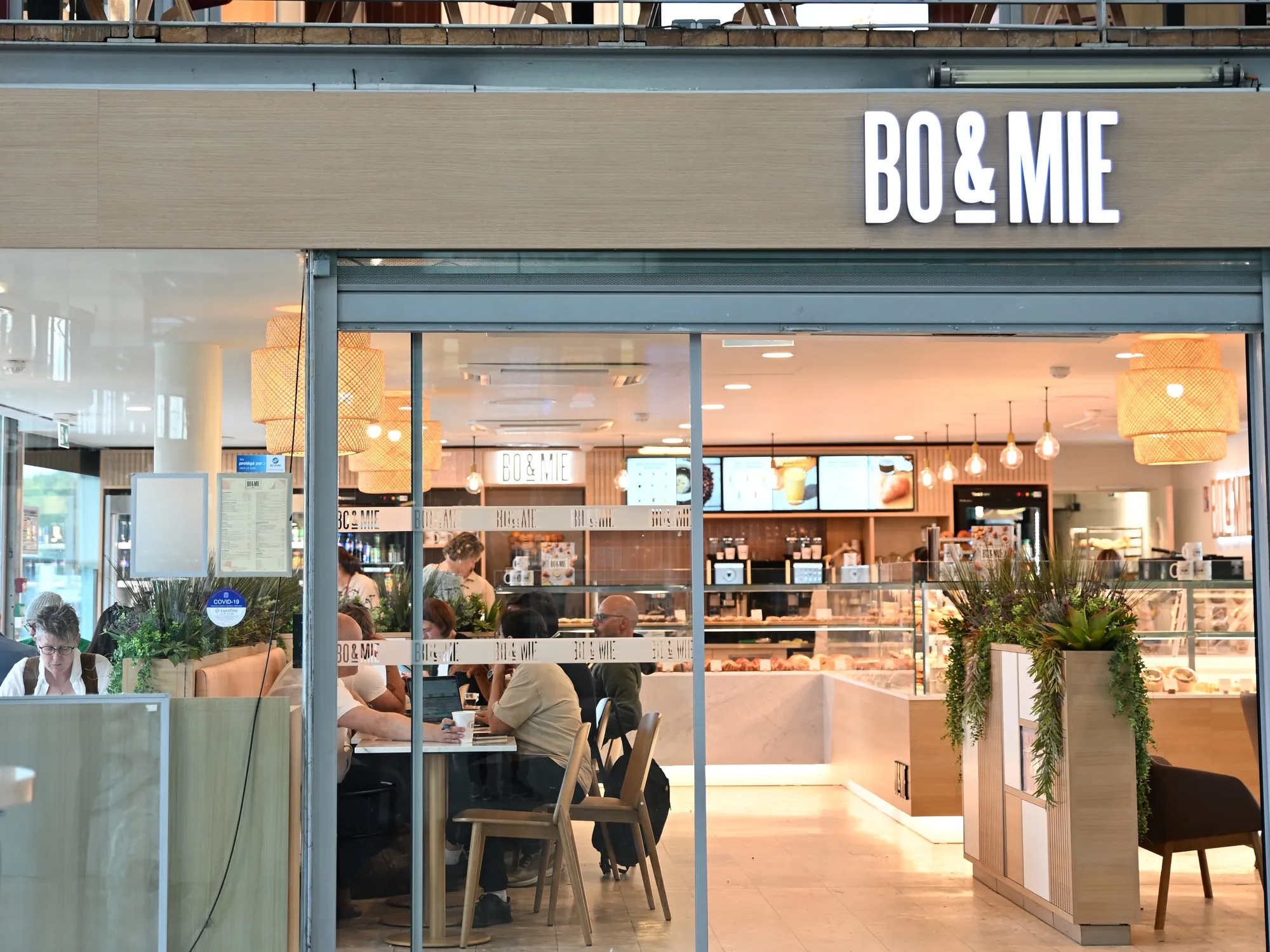 La devanture de BO&MIE Aix-en-Provence TGV dans le hall de la gare : l’enseigne lumineuse au-dessus des baies grandes ouvertes, et des voyageurs attablés à l’intérieur