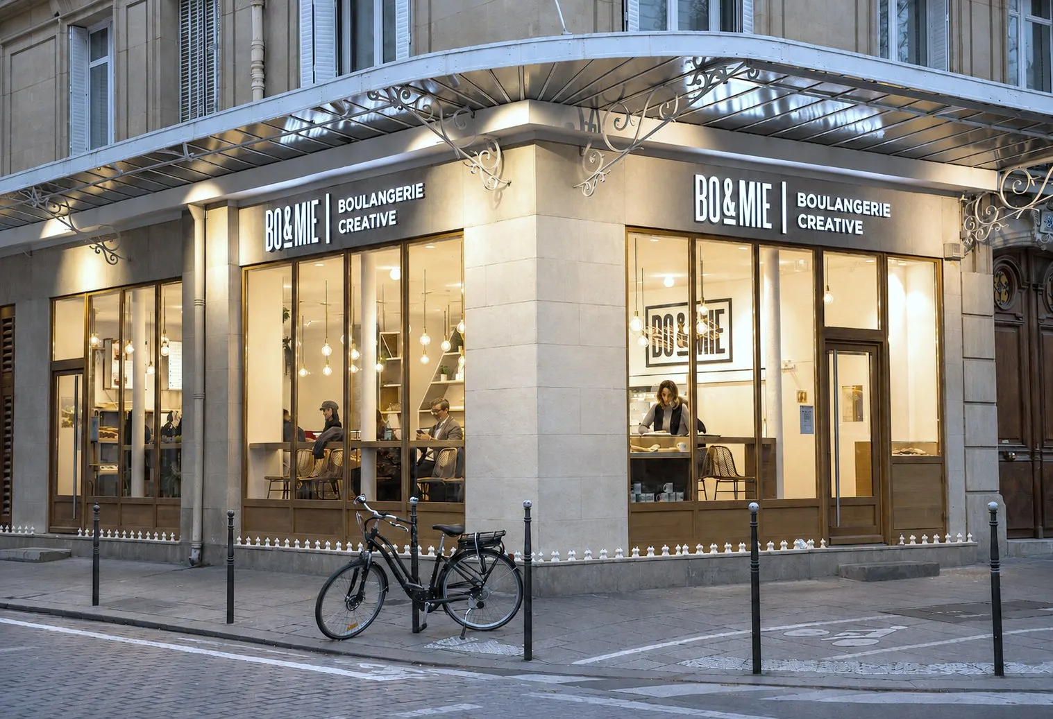 La devanture d’angle de BO&MIE Saint-Martin au crépuscule, enseignes « Boulangerie créative » allumées et clients en salle
