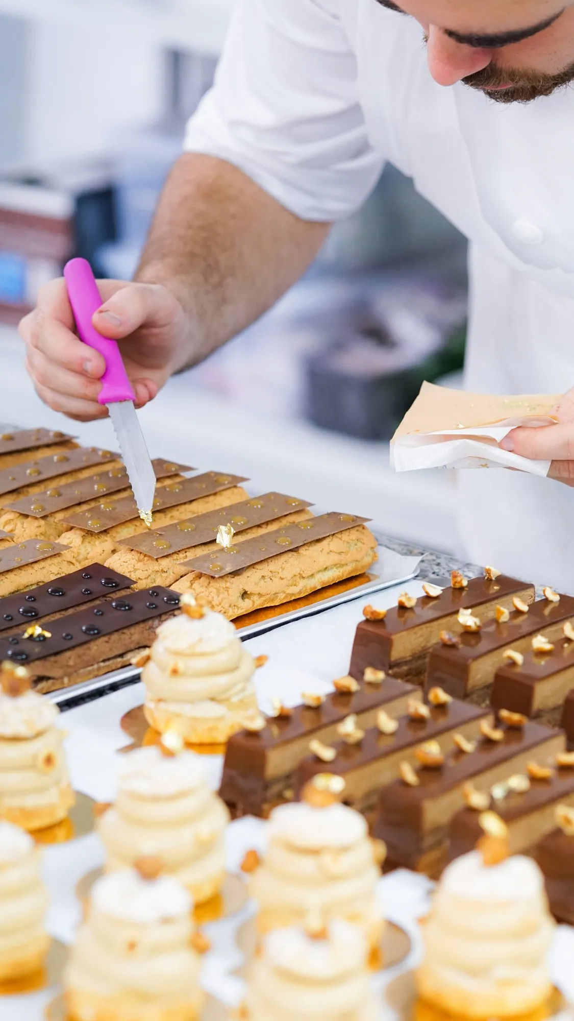 Un pâtissier pose une feuille d'or à la pointe du couteau sur une rangée d'éclairs