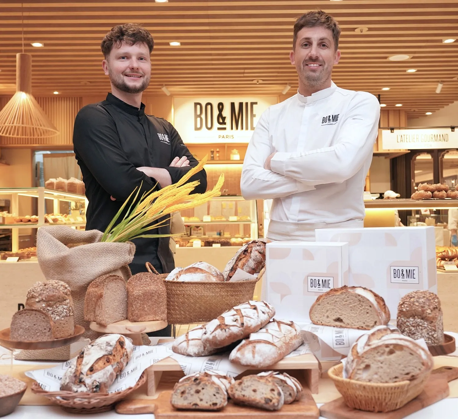 Deux boulangers BO&MIE, bras croisés devant un étal de pains et de coffrets, dans une boutique du réseau