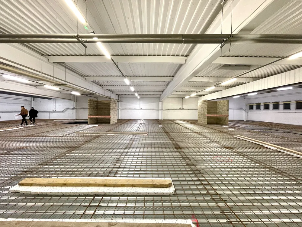 Le Lab de Clichy en chantier : la grande halle vide, le treillis d’armature au sol avant la dalle, deux personnes au fond
