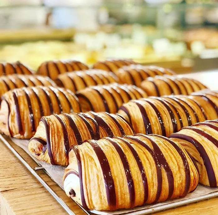 Des pains au chocolat BO&MIE alignés sur une grille, glaçage chocolat sur le feuilletage